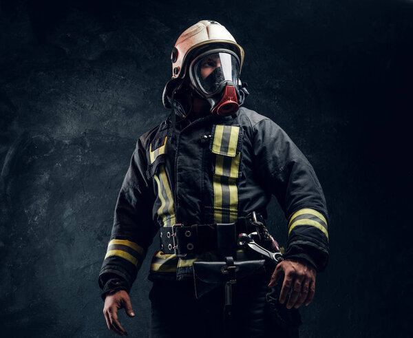 Portrait of a male in full firefighter equipment. Studio photo against a dark textured wall