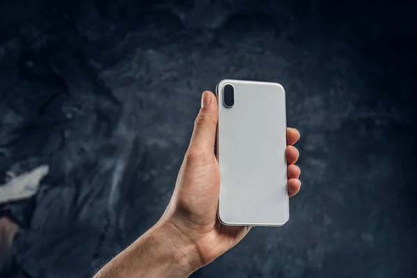 New modern smartphone with a beautiful design in mans hand against the background of the dark wall — Stock Photo, Image