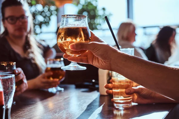 Young man holding a glass of beer sitting in a caf with his friends