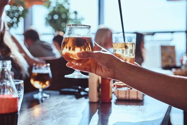 Joven sosteniendo un vaso de cerveza sentado en un café con sus amigos — Foto de Stock