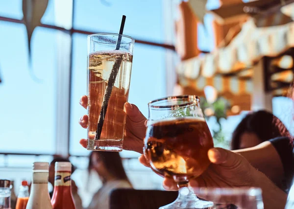 Amigos disfrutando de una cerveza en la cafetería al aire libre, tintineando con vasos de cerveza contra el cielo despejado — Foto de Stock