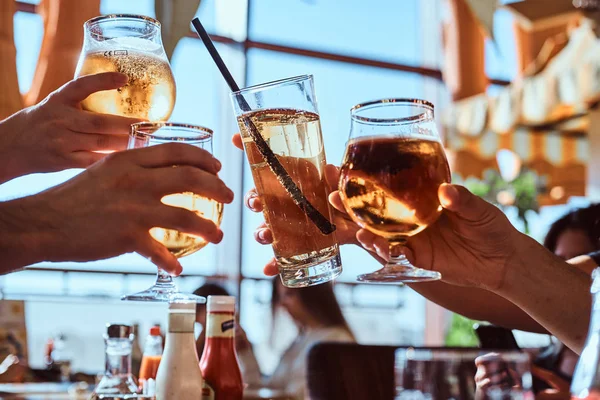 Amigos disfrutando de una cerveza en la cafetería al aire libre, tintineando con vasos de cerveza contra el cielo despejado — Foto de Stock