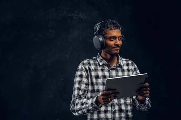 Ινδική άντρας σε ασύρματα ακουστικά κρατώντας ένα δισκίο και απολαμβάνει ακούει την αγαπημένη του μουσική στο studio — Φωτογραφία Αρχείου