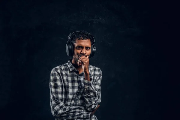Portret van een knappe Indiase man dragen een geruite shirt luistert naar muziek in draadloze hoofdtelefoons met doordachte look — Stockfoto