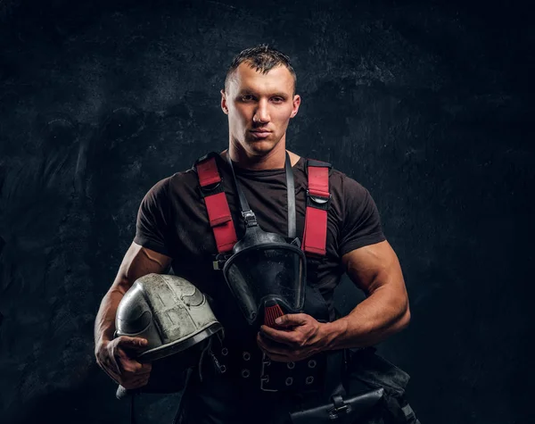 Brutal bombero mira a la cámara y sostiene un casco en su mano — Foto de Stock