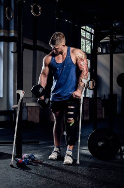 Bir spor salonu, bir koltuk değneği üzerinde yaslanmış bir dumbbell ile egzersizleri yapıyor ısınma profesyonel vücut geliştirmeci elinde, dövmeli.