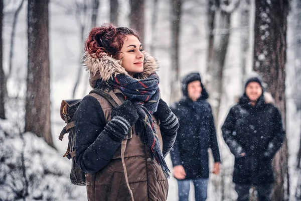 Schöne rothaarige Mädchen mit einem Rucksack zu Fuß mit seinen Freunden durch einen winterlichen Wald — Stockfoto