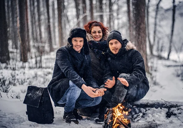 Eine Gruppe von Backpacker-Freunden unternahm eine Wanderung im verschneiten Wald, erwärmt am Feuer inmitten des Waldes sitzend — Stockfoto