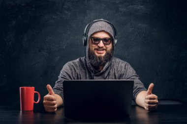 Memnun hacker bir karanlık duvara karanlık bir ofiste bir dizüstü bilgisayar arkasına oturur