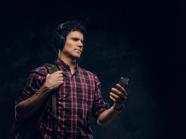 Vezeték nélküli fejhallgató fiatalember zenét hallgat, és tartja a smartphone egy stúdióban, a háttérben a sötét fal — Stock Fotó
