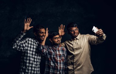 Bir sarılmak ve alma selfie smartphone cep telefonu ile rahat kıyafetler üç mutlu Hint arkadaş stand.