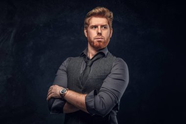 Şık giyinmiş Kızıl saçlı adam kollarını Studio bir karanlık dokulu duvara çarpı işareti ile poz