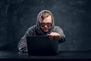 Programcı hoodie ve karanlık bir odada bir masada oturan dizüstü bilgisayarda parola kesmek güneş gözlüğü
