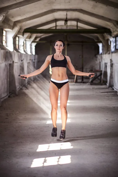 Όμορφη γυναίκα σε αθλητικά ενδύματα που κάνει άσκηση με το σχοινάκι στο εγκαταλελειμμένο βιομηχανικό κτίριο — Φωτογραφία Αρχείου
