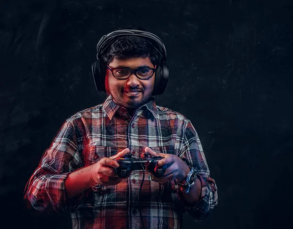 Indiano cara em fones de ouvido sem fio segurando joystick e joga jogos de vídeo no console de pé no estúdio — Fotografia de Stock