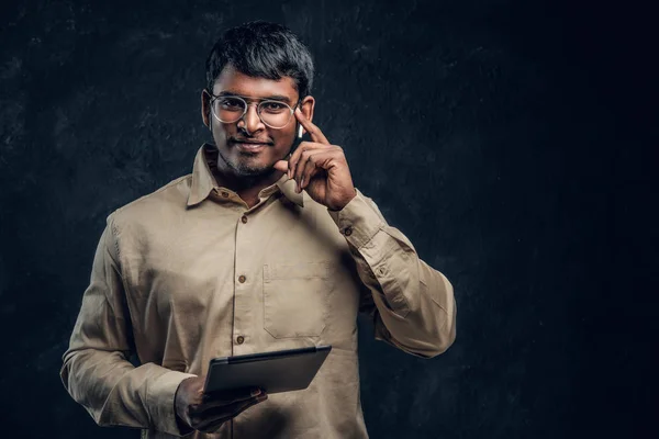 Confident Indian man  in eyewear and shirt holding a tablet computer and looking at a camera with a thoughtful look — Stock Photo, Image