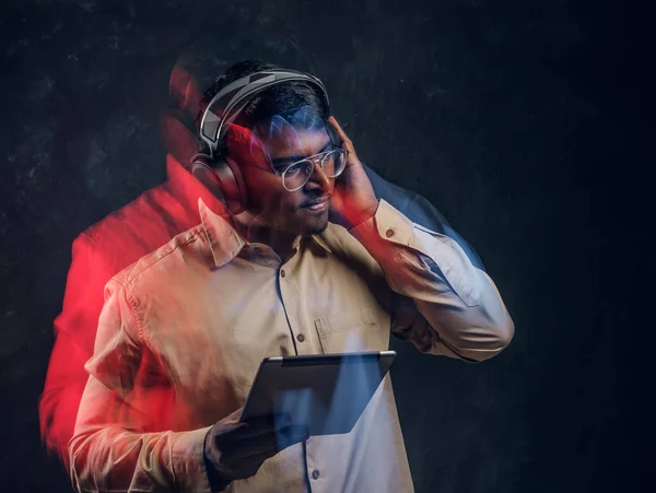 Hombre indio con auriculares inalámbricos sosteniendo una tableta y disfruta escuchando su música favorita en el estudio — Foto de Stock