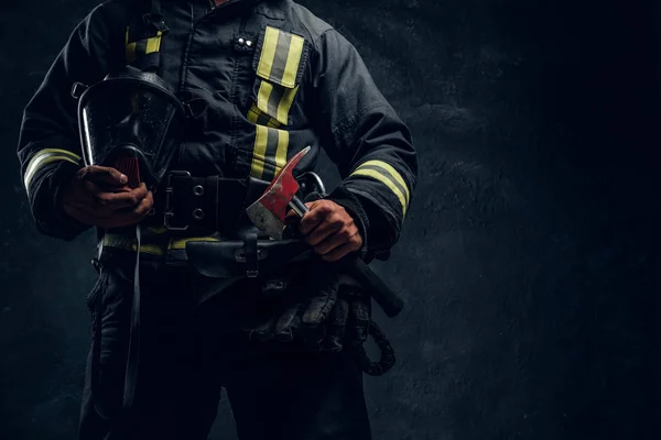 Skadrowana mężczyzna w mundurze, trzymając maskę tlenową i topór strażacki. Studio fotografii ścianę teksturowane ciemne — Zdjęcie stockowe