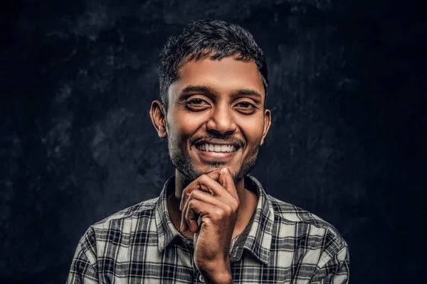 Jonge Indiase kerel het dragen van een geruite shirt die hand op kin, glimlachen en kijken naar een camera in een studio — Stockfoto