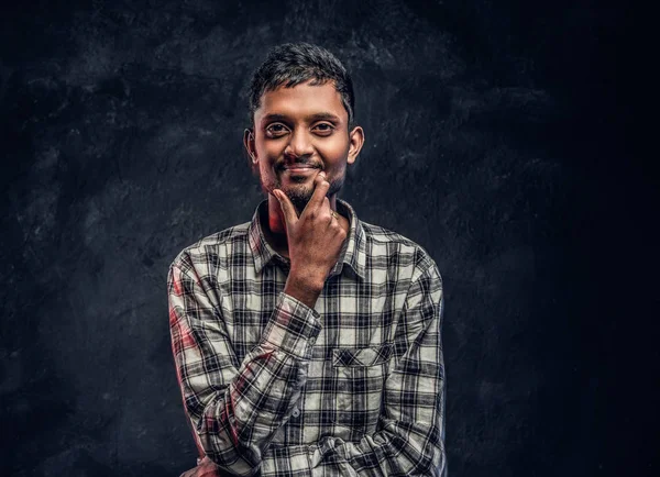 Retrato de um belo jovem indiano vestindo uma camisa quadriculada segurando a mão no queixo e olhando para uma câmera com um olhar pensativo — Fotografia de Stock