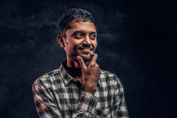 Knappe jonge Indiase kerel het dragen van een geruite shirt die hand op kin en zijwaarts op zoek met een peinzende blik — Stockfoto