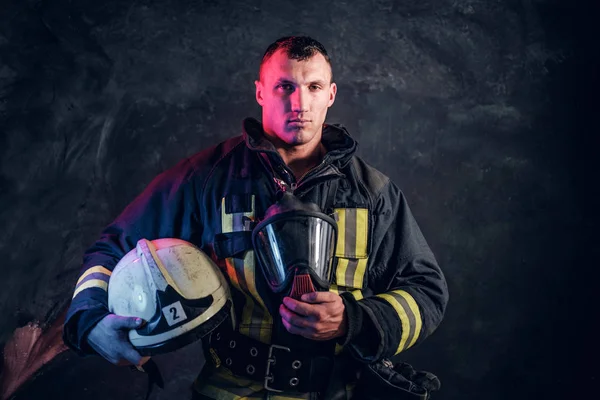 Brutal bombero mira a la cámara y sostiene un casco en su mano — Foto de Stock