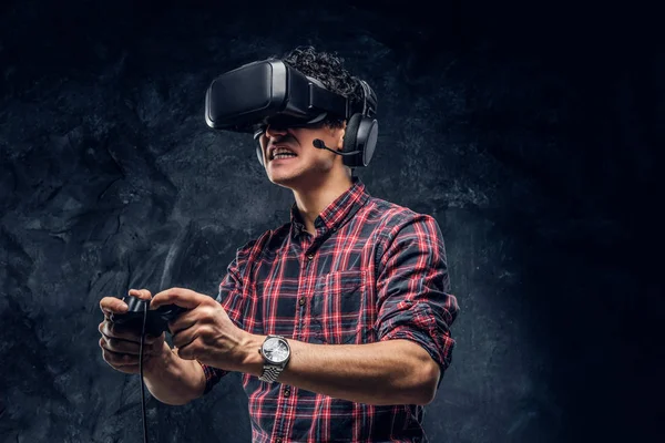 Emotionele man met behulp van Vr headset en het afspelen van een video game met joystick in een studio tegen de achtergrond van de donkere muur — Stockfoto