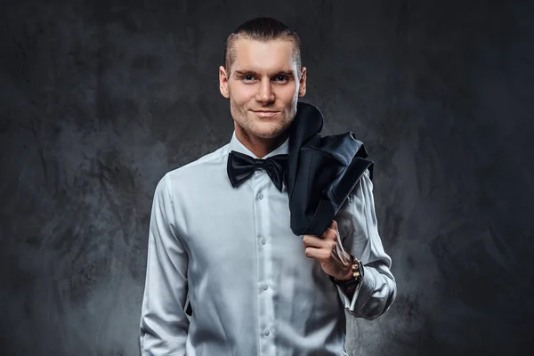 Elegantemente vestido homem bonito em camisa branca e gravata borboleta posando para uma câmera com jaqueta no ombro . — Fotografia de Stock