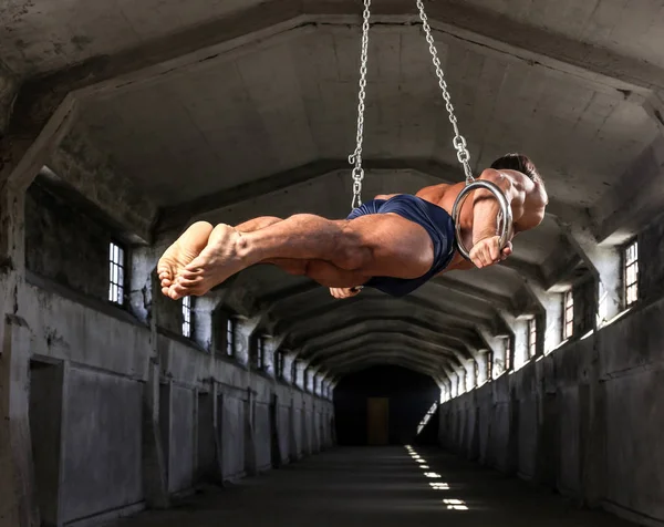 Een professionele sporter met een mooi gespierd lichaam traint op gymnastiek ringen in verlaten industrieel gebouw — Stockfoto