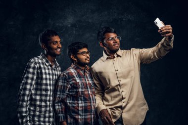 Bir sarılmak ve alma selfie smartphone cep telefonu ile rahat kıyafetler üç mutlu Hint arkadaş stand.