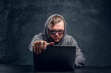 Programcı hoodie ve karanlık bir odada bir masada oturan dizüstü bilgisayarda parola kesmek güneş gözlüğü