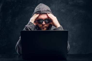 Oda karanlık bir duvara içinde laptop arkasına hoodie ve güneş gözlüğü dalgın hacker oturur 