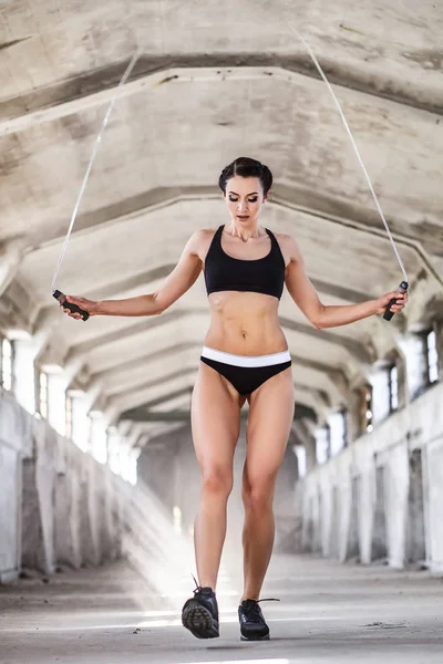 Piękna kobieta w sportowej robi ćwiczenia z skakanka w opuszczonych budynków przemysłowych — Zdjęcie stockowe