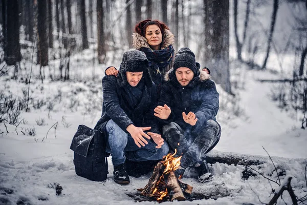 Eine Gruppe von Backpacker-Freunden unternahm eine Wanderung im verschneiten Wald, erwärmt am Feuer inmitten des Waldes sitzend — Stockfoto