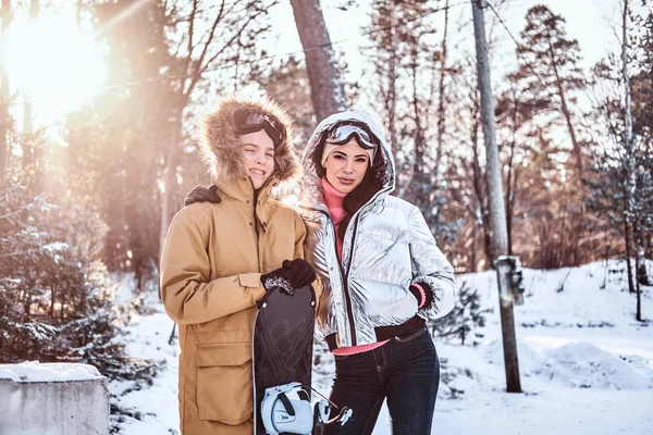 Sorrindo mãe e seu filho vestido com roupas quentes elegantes de pé no abraço na floresta nevada durante o nascer do sol — Fotografia de Stock