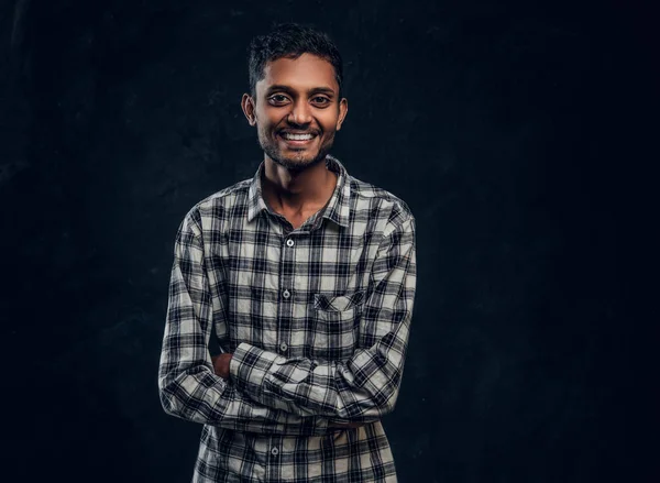 Porträtt av en leende indisk kille iklädd en rutig skjorta poserar med armarna korsade och tittar på kameran — Stockfoto