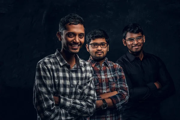 Portret van een drie Indiase studenten het dragen van casual kleding tegen een donkere getextureerde muur. — Stockfoto