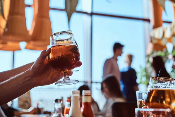 Giovane uomo che tiene un bicchiere di birra seduto in un caffè con i suoi amici — Foto Stock