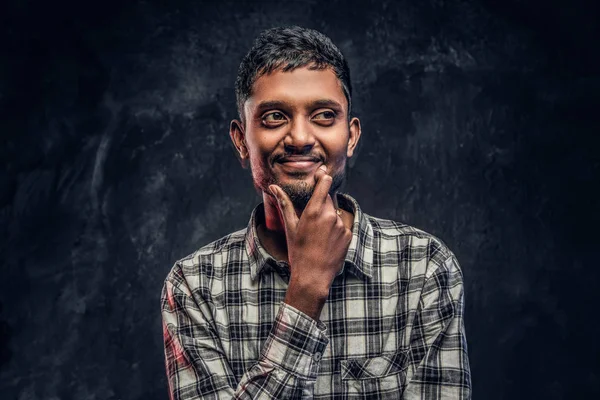 Knappe jonge Indiase kerel het dragen van een geruite shirt die hand op kin en zijwaarts op zoek met een peinzende blik — Stockfoto