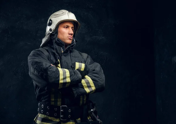 Portrait of a fireman in uniform and helmet stands with crossed hands, looking sideways with a confident look. — Stock Photo, Image