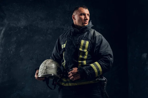 Brutal firefighter looks sideways and holds a helmet in his hand — Stock Photo, Image