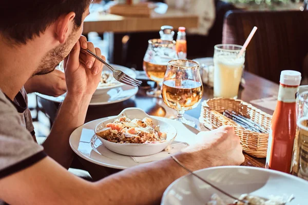 En ung man med hans vänner äta en fräsch och hälsosam sallad i en utomhus caf under lunchrast — Stockfoto