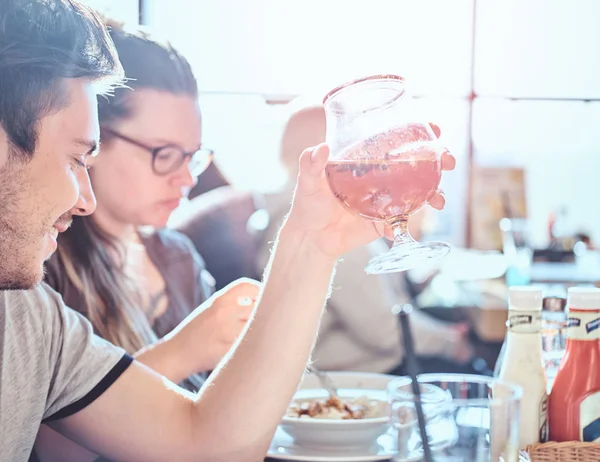 Ung man håller ett glas öl sitter i ett caf med hans vänner — Stockfoto