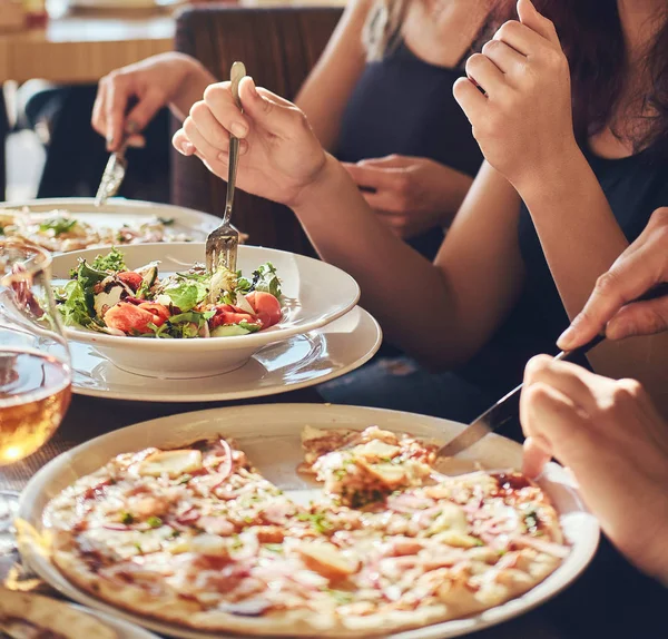 Young friends students eat pizza and salads in an outdoor caf during lunch break