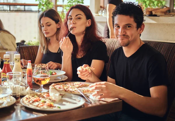 Jóvenes amigos alegres disfrutando de la comida y divirtiéndose juntos en el restaurante o cafetería al aire libre — Foto de Stock