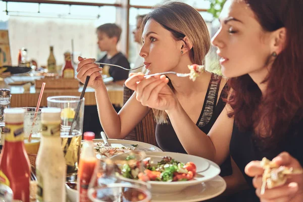 Dos chicas comen ensaladas sentadas con sus amigos en el café durante el almuerzo — Foto de Stock