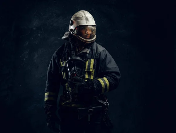 Retrato de um homem em equipamento de bombeiro completo posando em um estúdio escuro — Fotografia de Stock