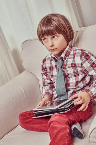 Het dragen van een geruite shirt zittend op een bank met aantal tabletten thuis schooljongen — Stockfoto