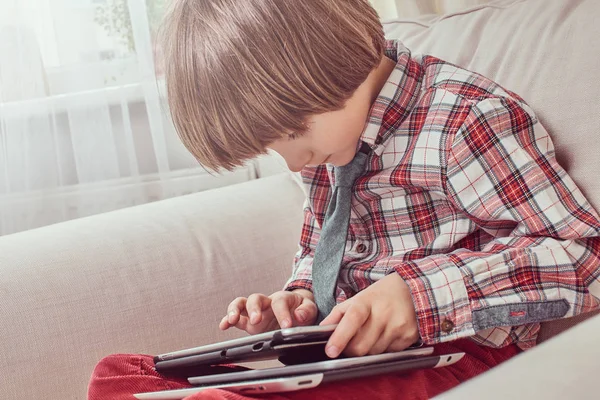 Kaukasiska skolpojke bär en rutig skjorta med slips med hjälp av en digital tablett som sitter på en soffa hemma — Stockfoto