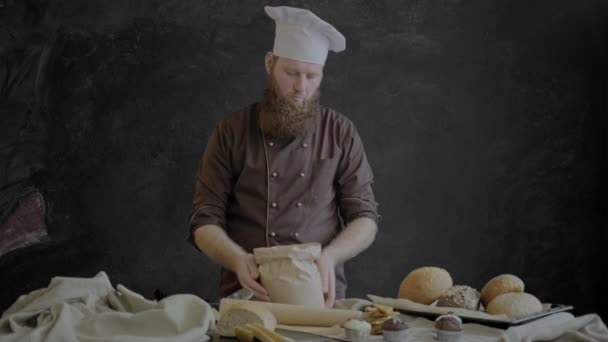 Kocken kontrollerar kvaliteten på mjölet, stående nära en tabell dekorerad med bakverk av sitt bageri. — Stockvideo